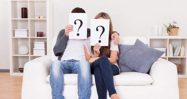Paar auf Sofa mit Fragezeichen vor dem Kopf