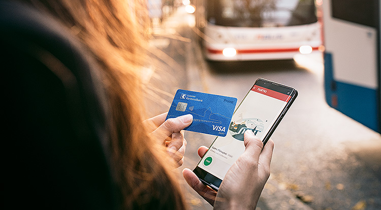Eine Frau an Bushaltestelle mit Debitkarte und Smartphone in der Hand